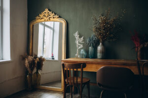 a room interior with a vintage mirror and dark wood desk and chair